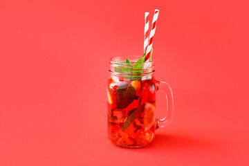 Mason jar of tasty ice tea with fruits on color background