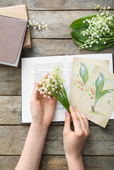 Female hands with beautiful lily-of-the-valley flowers and greeting cards on wooden background