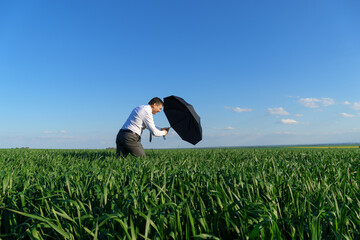 businessman poses with umbrella in a field, he's falling, a concept of crisis, green grass and blue...