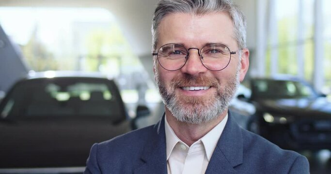 Positive male dealer in eyewear and suit posing at modern car center. Successful career and auto business concept. Close-up.