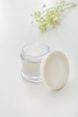 Jar of cream and lily-of-the-valley flowers on light background