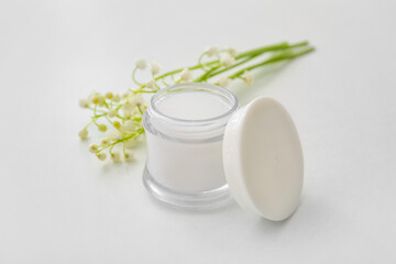 Jar of cream and lily-of-the-valley flowers on light background