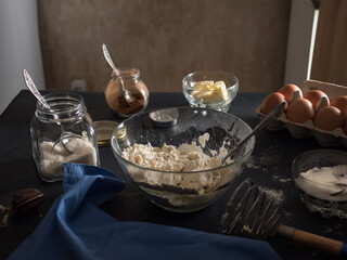Cooking a cake. On the table are ingredients for making a pie (flour, eggs, cocoa, butter, sugar, salt), kitchen utensils and textiles. Dark background