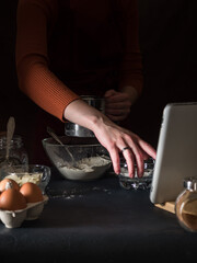 Cooking a cake according to the recipe. We look at the recipe in an electronic tablet. On the table are ingredients for making a pie  kitchen utensils, a white tablet. Dark background