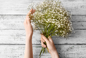 Female hands with beautiful gypsophila flowers on light wooden background