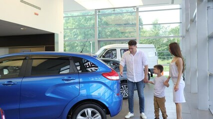 A beautiful couple with a young son is walking around the salon of a car dealership, looking at cars, picking up a vehicle for purchase. A family in a car dealership. Family purchase of a new car