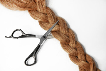 Scissors cut a long braid of hair on a white background