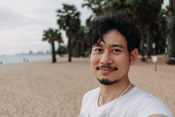 Happy Asian man take selfie with palm tree on the beach. Summer travel concept.