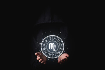 A woman in a black mantle with her palms holds the glowing astrological signs of the zodiacs on a black background
