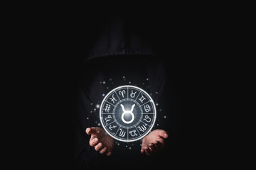 A woman in a black mantle with her palms holds the glowing astrological signs of the zodiacs on a...