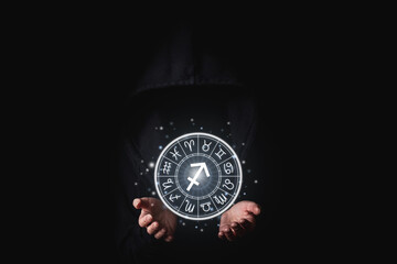 Women's hand in the dark holding glowing astrological signs of the zodiac in a circle