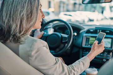 Rear view of mature beautiful woman in smart casual wear using phone while driving car