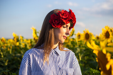 Young woman in a wreath of red flowers on a sunflower field