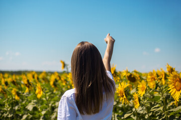 Young woman in white t-shirt points a finger at the horizon on a sunflower field on a summer sunny day