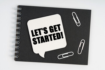 On the notebook are white paper clips and a sign with the inscription - Let s get started