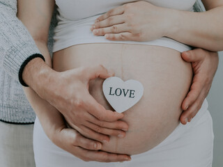 A man holds a heart and belly of a pregnant woman.
A man holds a wooden heart with the inscription: love and belly of a pregnant woman, close-up side view.