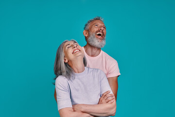 Happy senior couple bonding and laughing while standing together against blue background