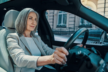 Fototapeta na wymiar Mature beautiful woman in smart casual wear smiling while driving car