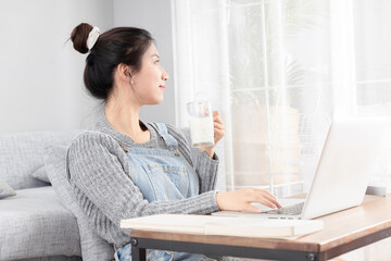 Asian girl sitting on the carpet, taking online class and drinking milk