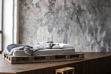 Unfilled bed made of wooden blocks with beige bedding in the bedroom against a wall with venetian stucco. Scandinavian style