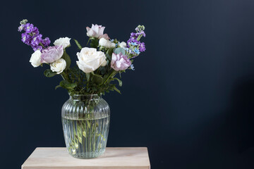 Bouquet of hackelia velutina, purple and white roses, small tea roses, matthiola incana and blue iris in glass vase opposite on black background.