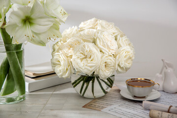 A bouquet of white roses in a round glass vase on a table with a cup of tea and a book. Copy space. - Powered by Adobe