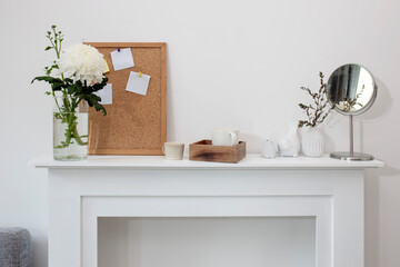 A chrysanthemum in a transparent vase, a cork board with empty leaves, a wooden tray with a cup of coffee, a vase with eucalyptus, a mirror and a figurine of birds. Scandinavian style.
