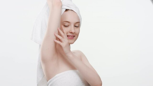 Good-looking young slim European woman wrapped in a towel touches her body and looks at the camera on white background | Skin rejuvenation concept