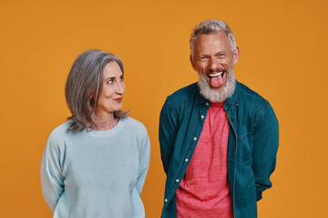 Obraz premium Beautiful senior couple laughing while standing together against orange background