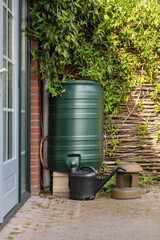 Green rain barrel and a watering can to collect rainwater and reusing it to water the paints and...