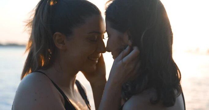 Lesbian girlfirens are happy in golden hour, beach. Kissing young woman, LGBTQ, equality and togetherness concept in a romantic place. Gay couple.