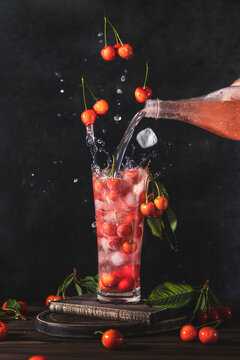Glass of many cherry or merry berries with lemonade water splesh, fly berries and ice, pouring lemonade from bottle to glass surround of fresh cherry or merry berries