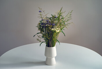 A bouquet of wild flowers in a white vase on a table on a gray background.