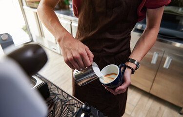 Close-up of professional barista pouring steamed milk into coffee cup making latte behind bar counter