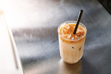 High angle view of an iced coffee latte with straw on a steel counter top in coffee house.