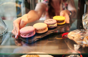 Close-up of a cafeteria worker taking colorful macarons from a showcase in pastry store