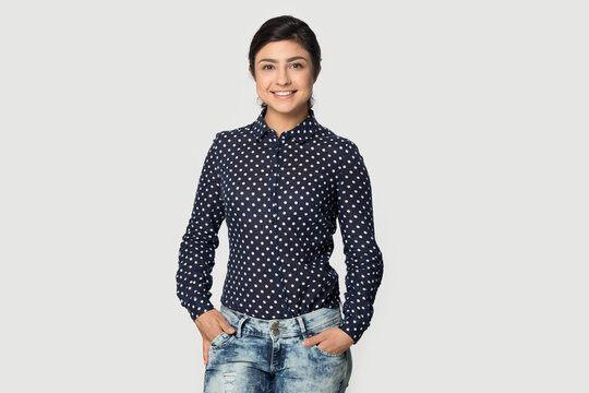 Portrait of smiling millennial mixed race ethnicity female stand isolated on grey studio background. Happy young Indian woman in trendy fashion clothes feel confident. Employment, style concept.