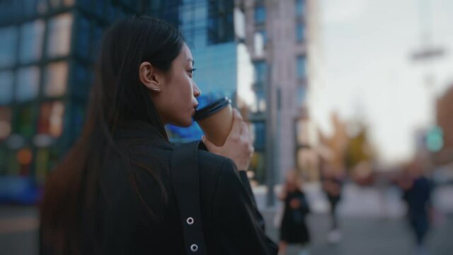 Attractive brunette young business woman walking in downtown at sunset. Following a beautiful mxied-race girl going to work, drinking coffee and using phone.