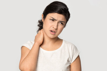 Unhealthy young Indian woman isolated on grey studio background massage neck suffer from backache. Unwell tired millennial mixed race female struggle with muscular back spasm strain or pain.