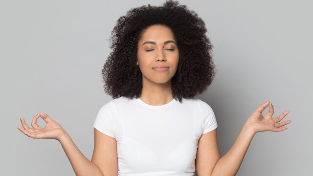 Calm millennial African American woman isolated on grey studio background practice yoga breathe fresh air. Peaceful young biracial female meditate relieve negative emotions. Stress free concept.