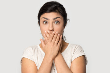 Headshot portrait of stunned young Indian woman feel shocked by unexpected bad news message. Profile picture of unhappy ethnic female isolated on gray studio background surprised by negative notice.
