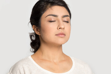 Close up of calm Indian woman isolated on grey studio background meditate breathe fresh ventilated conditioned air. Peaceful young ethnic female relieve negative emotion. Stress free concept. - obrazy, fototapety, plakaty