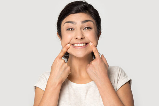 Headshot portrait of overjoyed Indian woman isolated on grey studio background show wide smile. Profile picture of happy young mixed race female feel optimistic excited. Humor, fun concept.
