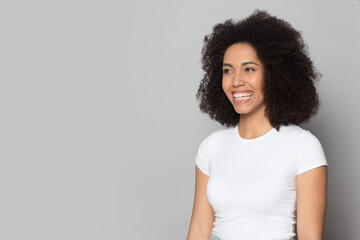 Smiling young African American woman isolated on grey studio background look at blank empty copy space. Happy mixed race female recommend good sale deal or promotion. Commerce concept.