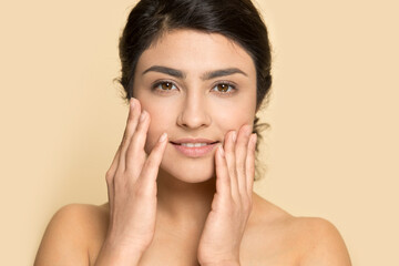 Portrait of young Indian woman isolated on yellow studio background touch healthy face skin after beauty salon procedures. Smiling mixed race female satisfied with facial treatment. Skincare concept. - Powered by Adobe