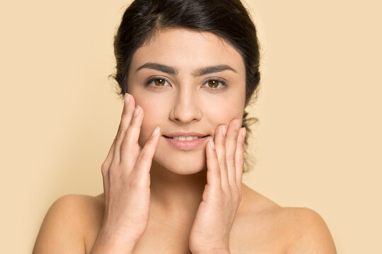 Portrait Of Young Indian Woman Isolated On Yellow Studio Background Touch Healthy Face Skin After Beauty Salon Procedures. Smiling Mixed Race Female Satisfied With Facial Treatment. Skincare Concept.