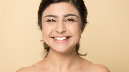 Close up portrait of smiling Indian woman isolated on yellow studio background show healthy glowing face skin after treatment procedures. Happy mixed race female with white teeth. Skincare concept.