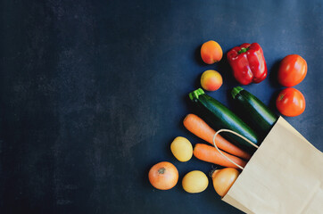 Shopping or delivery healthy food concept. Food supermarket and clean vegan eating concept. Fresh vegetables and fruits: carrot, potato, zucchini, tomato in paper bag on black background. Copy space.