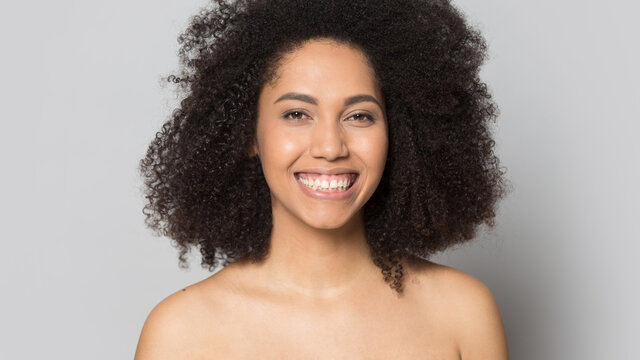 Headshot portrait of young African American naked woman isolated on grey studio background show natural no makeup beauty. Profile picture of happy mixed race female with healthy soft face skin.