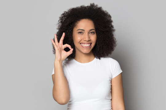 Profile picture of smiling African American woman isolated on grey studio background show ok sign. Headshot portrait of happy millennial mixed race female demonstrate all right hand gesture.